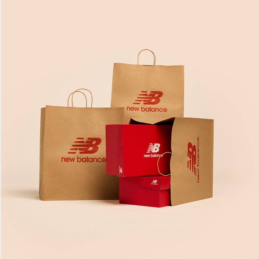 Multiple brown paper New Balance shopping bags on a tan studio backdrop.